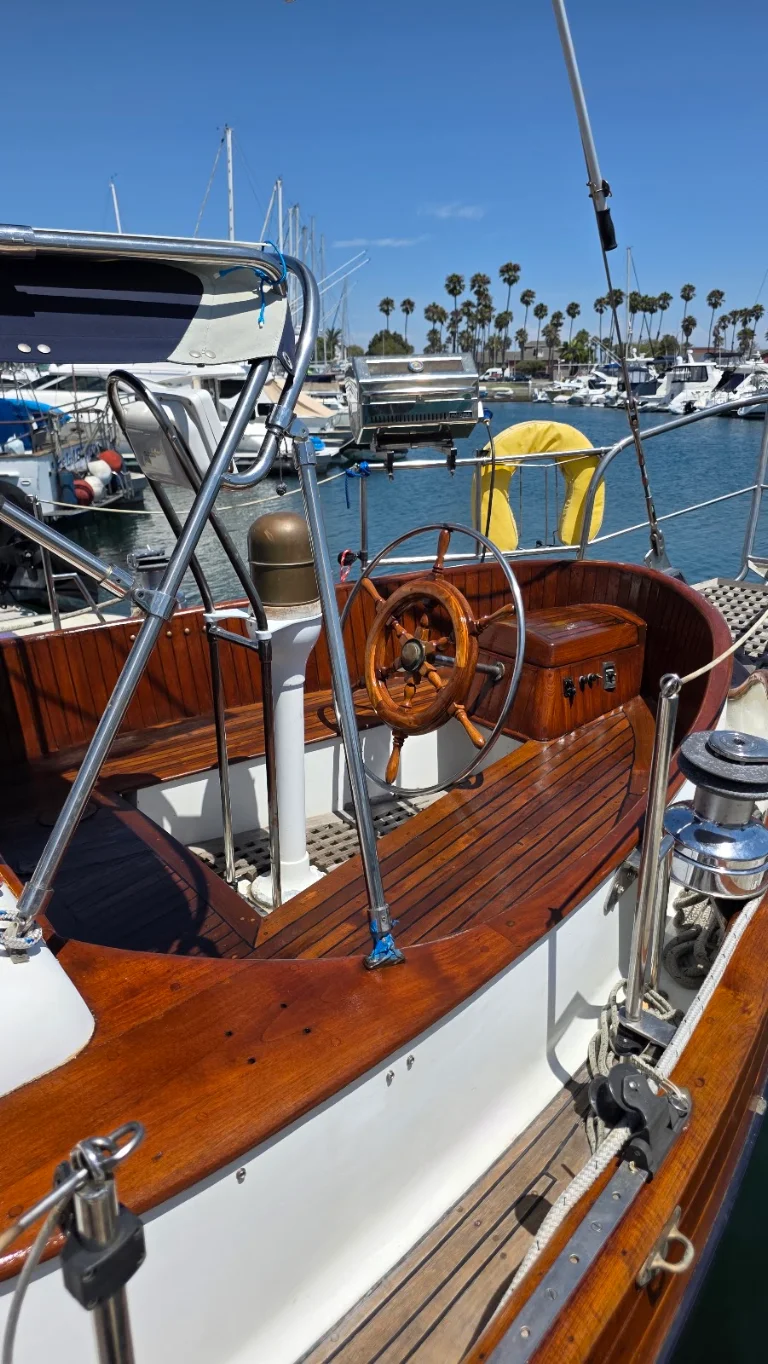 Classic wooden sailboat teak cockpit restoration at a marina lined with palm trees